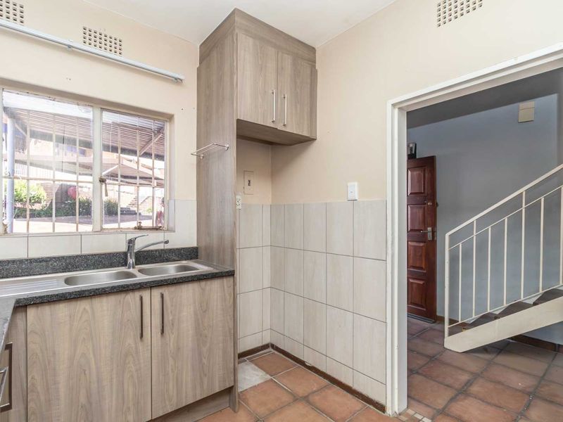 A functional kitchen area featuring laminate cabinetry, granite countertops, a double sink, and tiled splashbacks, with direct access to the hallway and staircase.