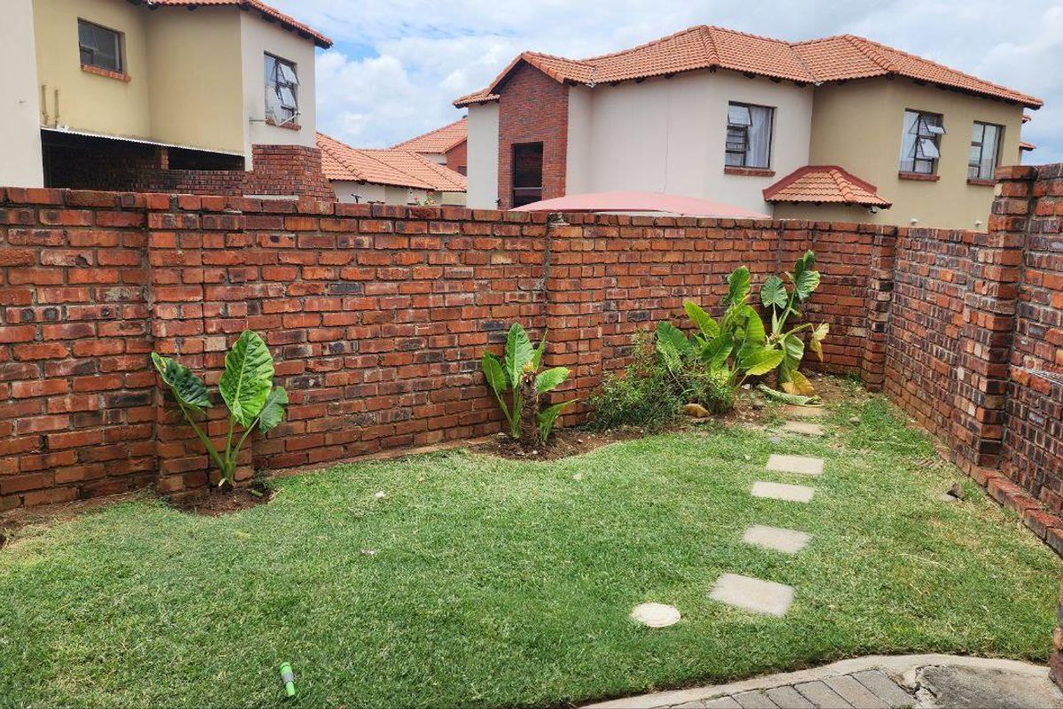 A private rear garden featuring a lawn, stone stepping path, and perimeter face-brick boundary walls.