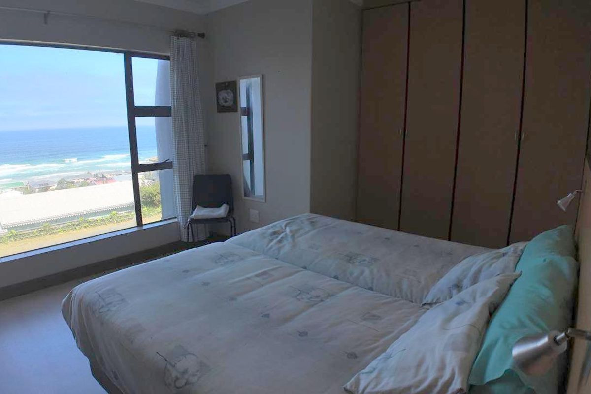 A bedroom featuring built-in cupboards and a large window offering expansive ocean views.