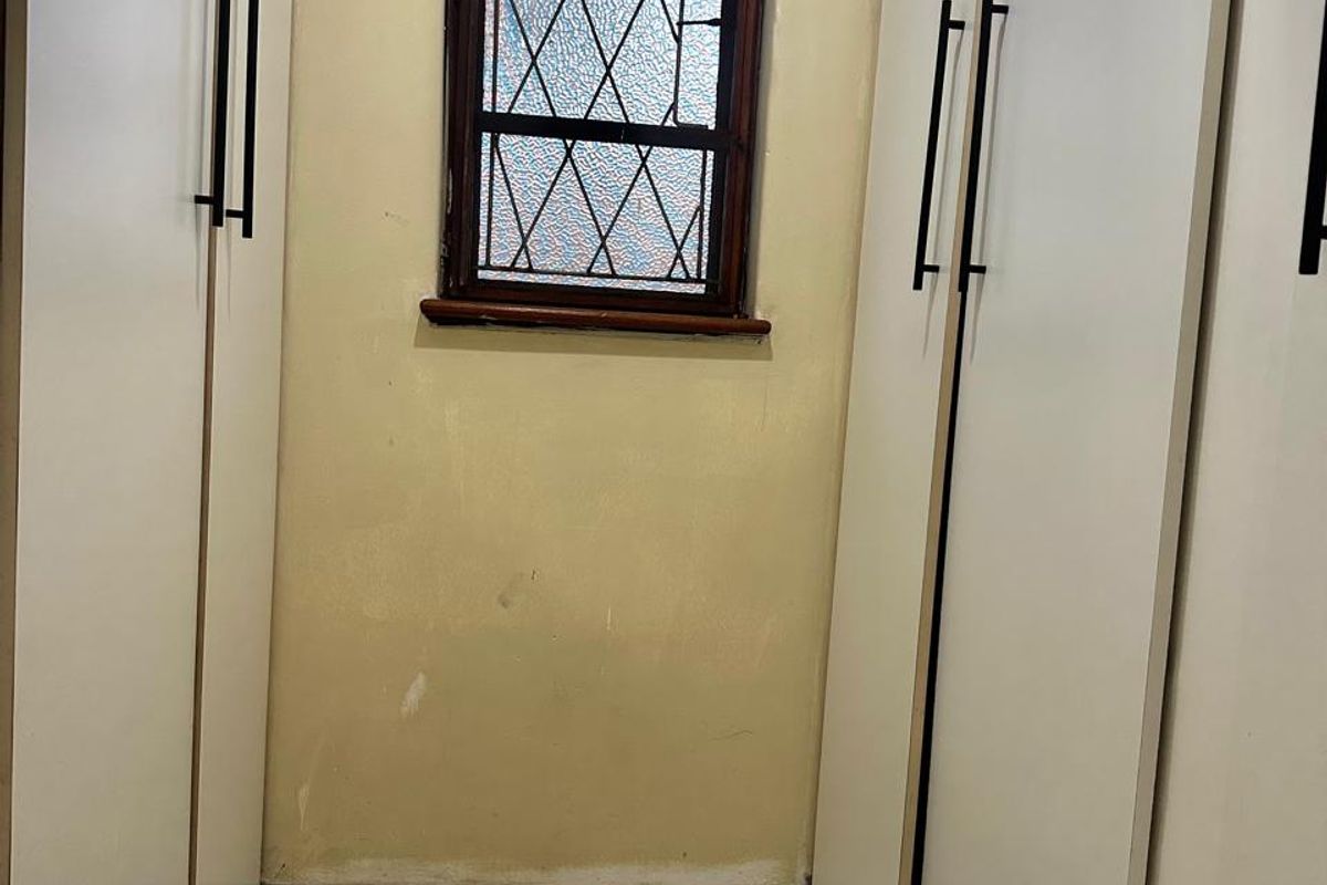 A small dressing area or bedroom space featuring built-in cupboards, tiled flooring, and a classic leaded glass window.