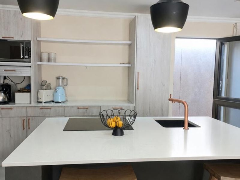 Modern kitchen featuring a central island with a cooktop, integrated sink, copper faucet, and contemporary pendant lighting.