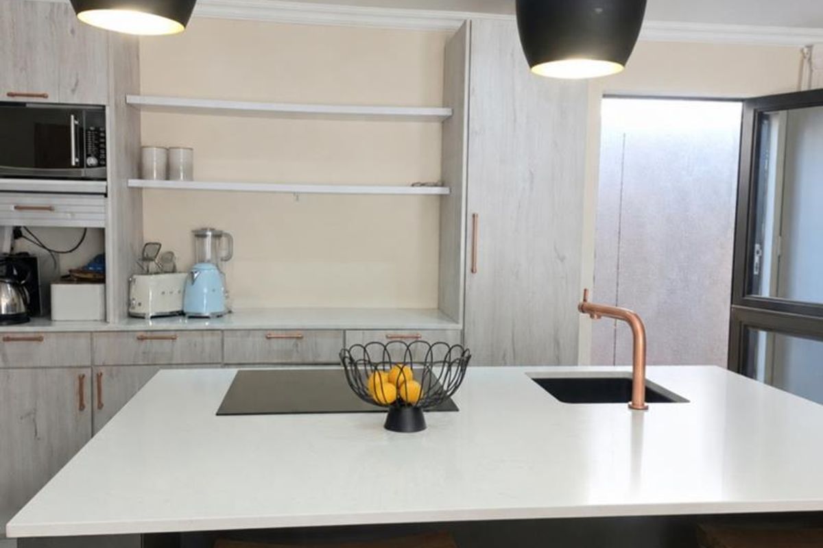 Modern kitchen featuring a central island with a cooktop, integrated sink, copper faucet, and contemporary pendant lighting.