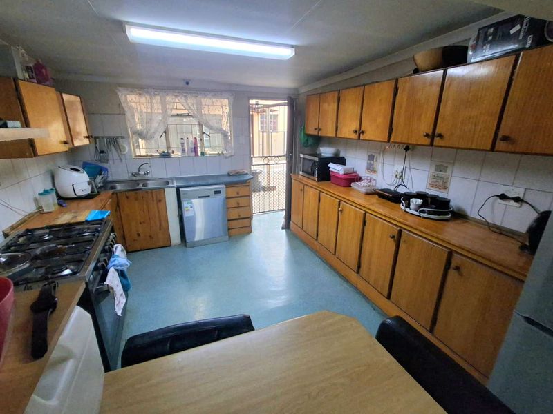 A functional kitchen featuring extensive wooden cabinetry, laminate countertops, a gas hob, and a double bowl sink with direct access to the exterior.