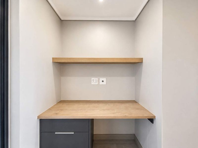 A clean, modern built-in study nook featuring a wood-finish desk, floating shelf, and integrated drawer storage with electrical connectivity.
