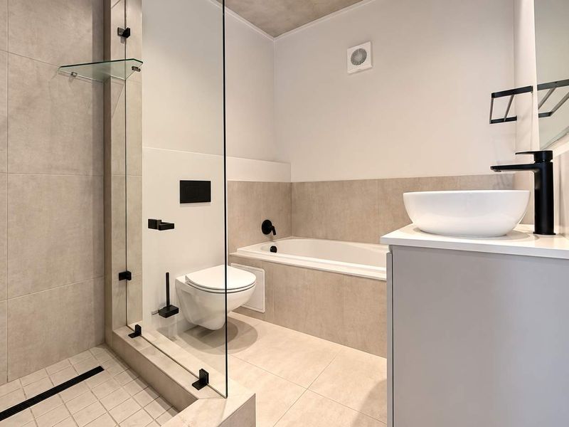Modern bathroom featuring a walk-in shower with glass screen, built-in bathtub, wall-mounted toilet, and a vanity with a vessel sink and matte black fixtures.