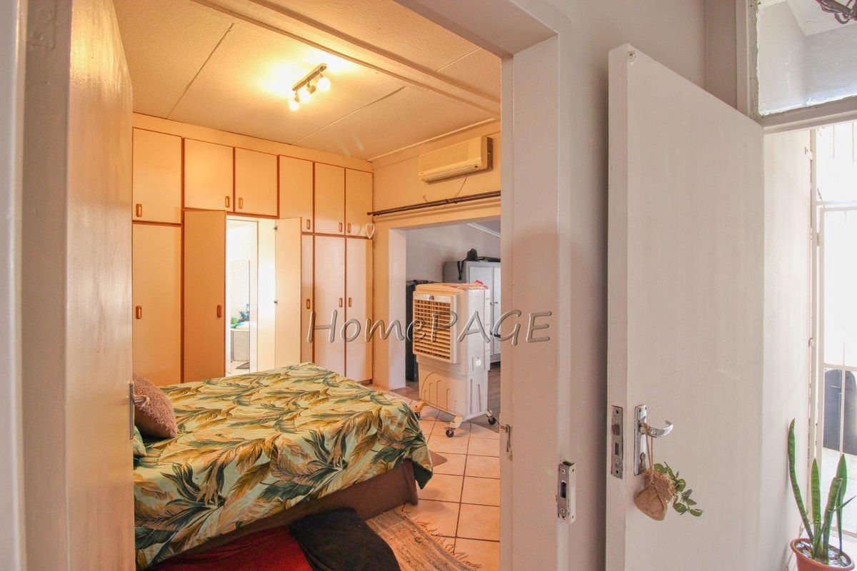 A bedroom featuring extensive built-in floor-to-ceiling cabinetry and a wall-mounted air conditioning unit, with an adjoining space visible through the doorway.