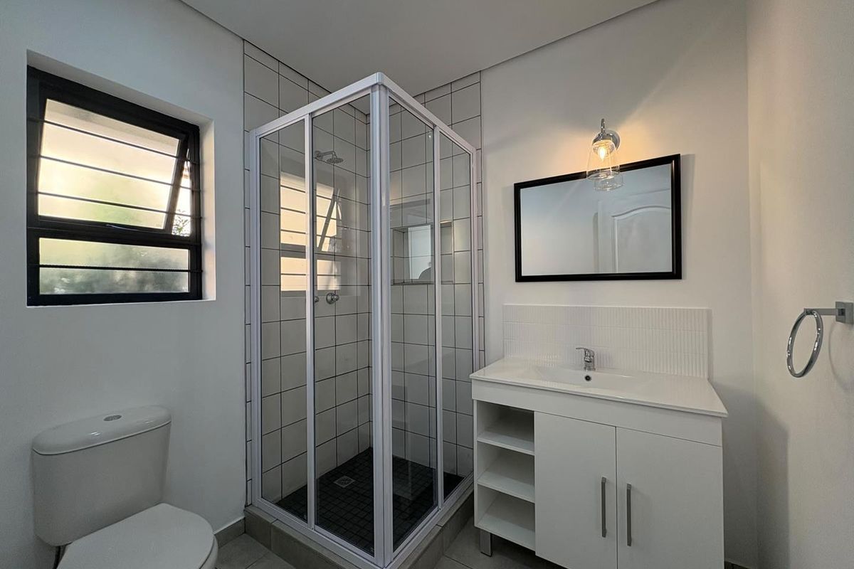 A clean, modern bathroom featuring a corner shower enclosure, white vanity cabinet with basin, and neutral floor and wall tiling.