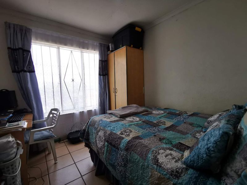 A bedroom featuring tiled flooring, security bars on the window, and a built-in wardrobe, requiring cosmetic updates to the wall finishes.