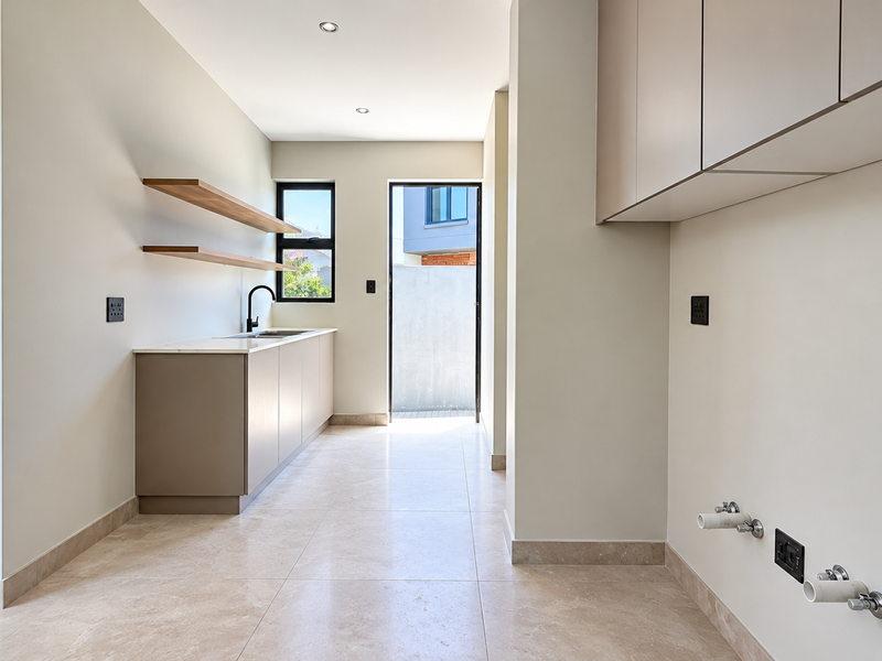 A modern, clean scullery featuring built-in cabinetry, stone countertops, floating timber shelves, and dedicated plumbing connections for laundry or kitchen appliances.