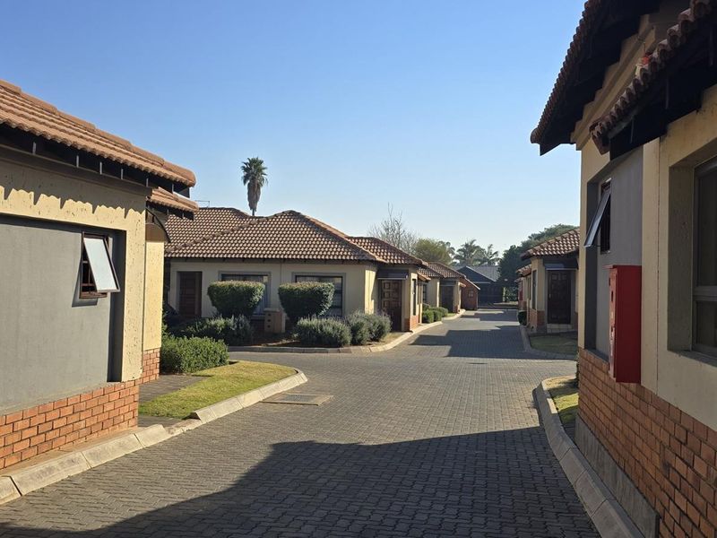 A view of the townhouse complex driveway featuring paved roads, brick and plaster facades, and tiled roofing.