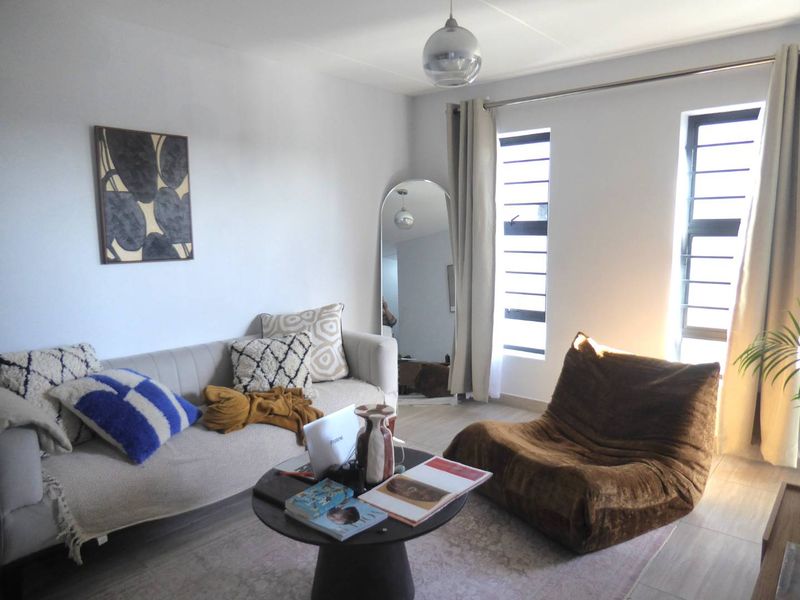 A bright living room featuring tiled flooring, louvered windows allowing natural light, and a modern pendant light fixture.