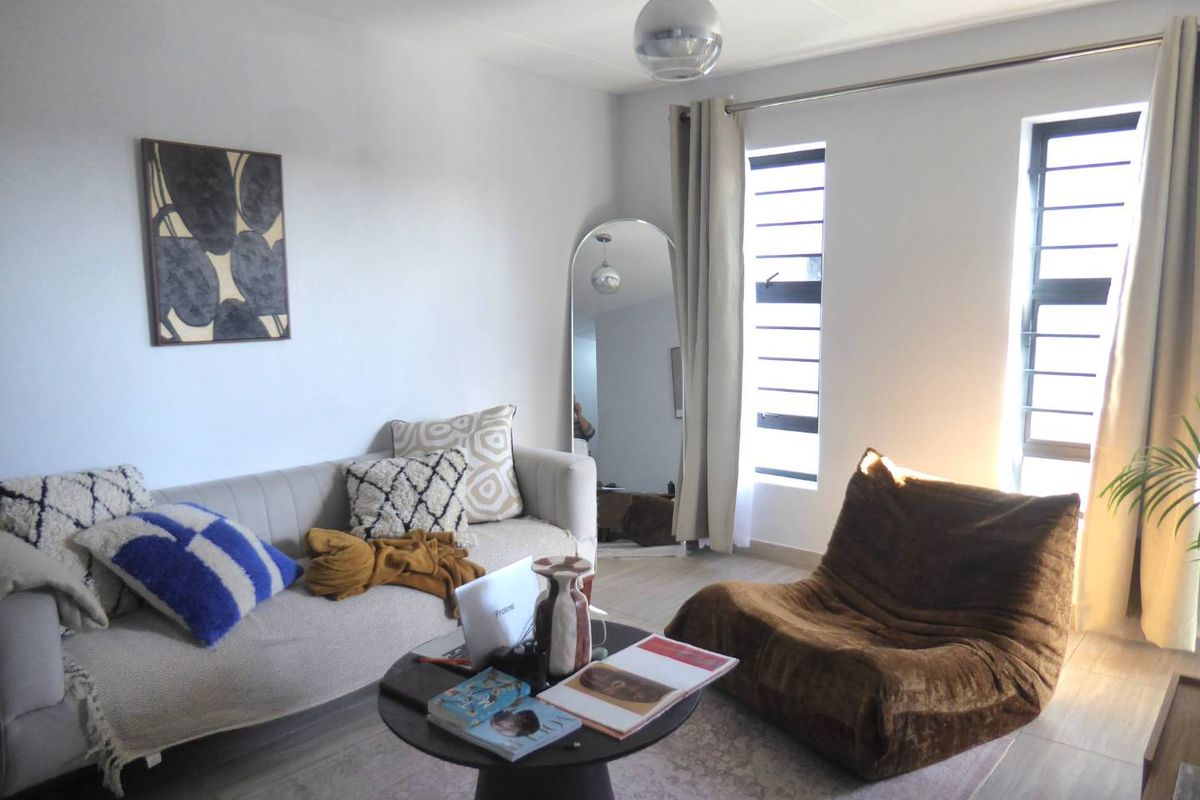 A bright living room featuring tiled flooring, louvered windows allowing natural light, and a modern pendant light fixture.