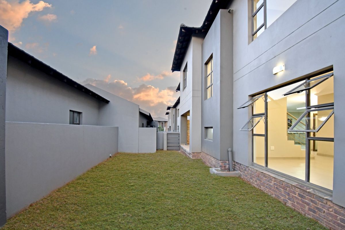 A view of the rear exterior of the property featuring a manicured lawn, plastered walls with brick detailing, and modern aluminium window frames.