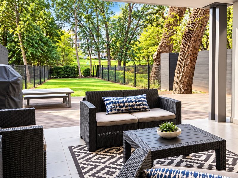 A well-maintained covered patio featuring tiled flooring, transitioning to a timber deck overlooking a private garden area with mature trees.