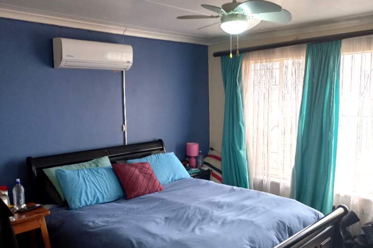 A bedroom featuring a wall-mounted air conditioning unit, a ceiling fan, and tiled flooring with large windows.