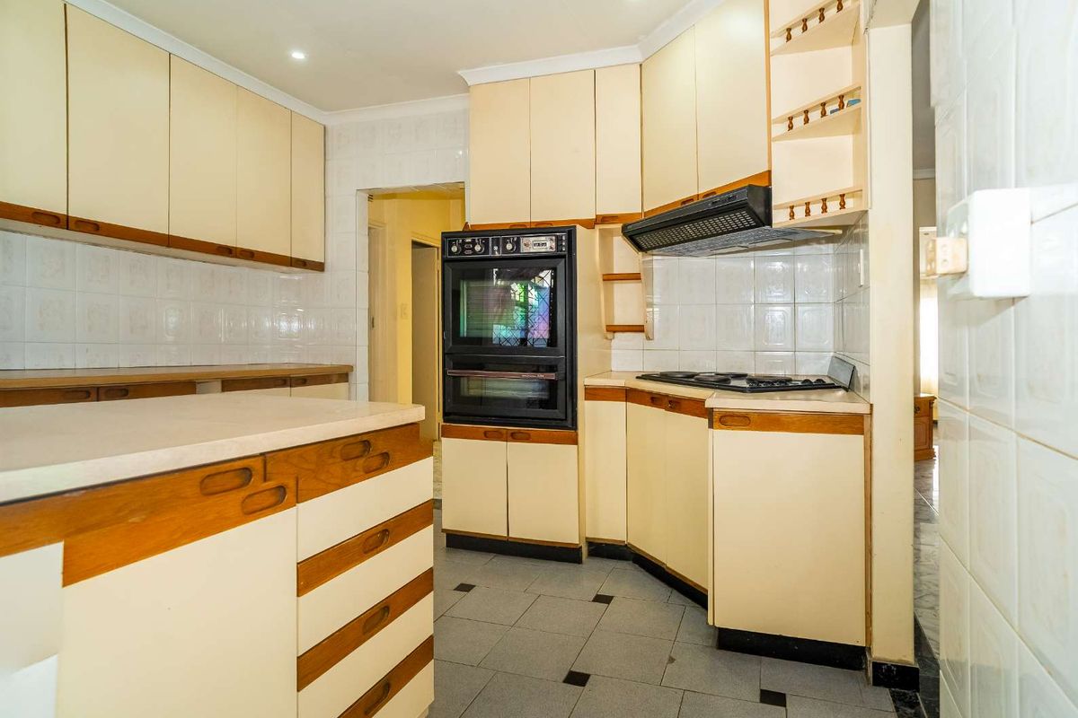 A functional kitchen featuring built-in cabinetry, a double oven, a hob, and an extractor fan with tiled splashbacks and flooring.
