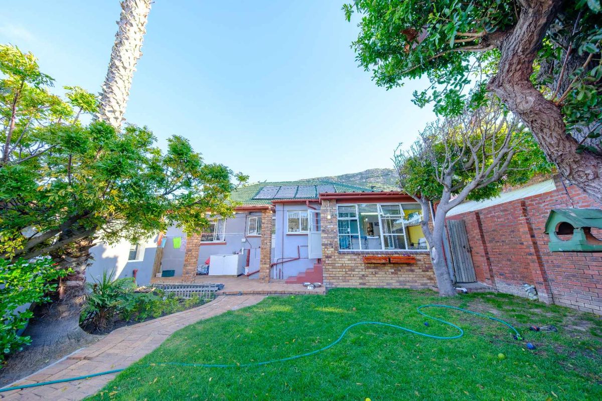 Rear view of the property featuring a brick and rendered facade, established garden, paved walkway, and solar water heating panels on the roof.