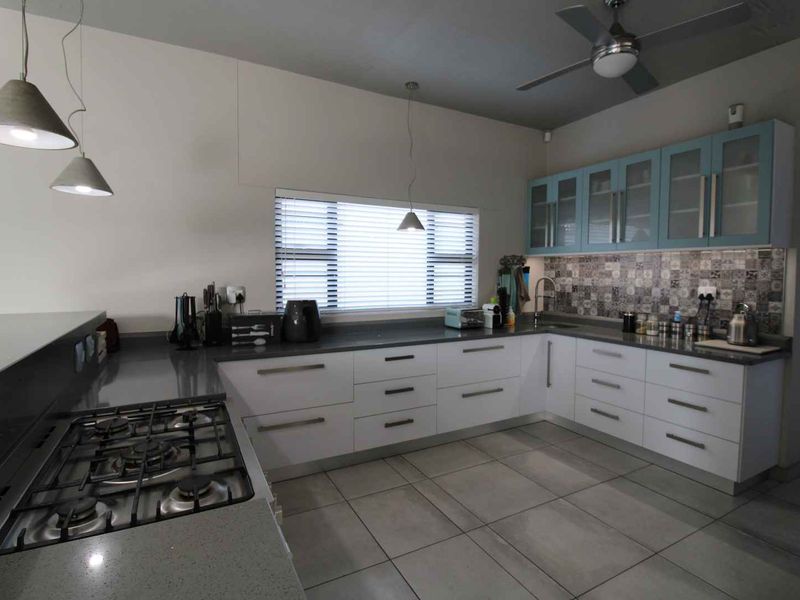 Modern kitchen featuring stone countertops, gas hob, ample built-in cabinetry with glass-fronted uppers, decorative tiled backsplash, and contemporary pendant lighting.