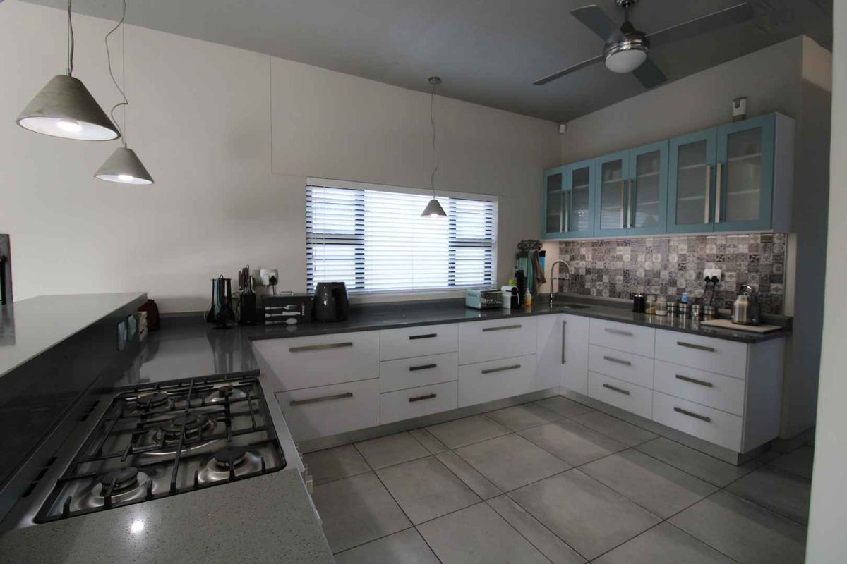 Modern kitchen featuring stone countertops, gas hob, ample built-in cabinetry with glass-fronted uppers, decorative tiled backsplash, and contemporary pendant lighting.