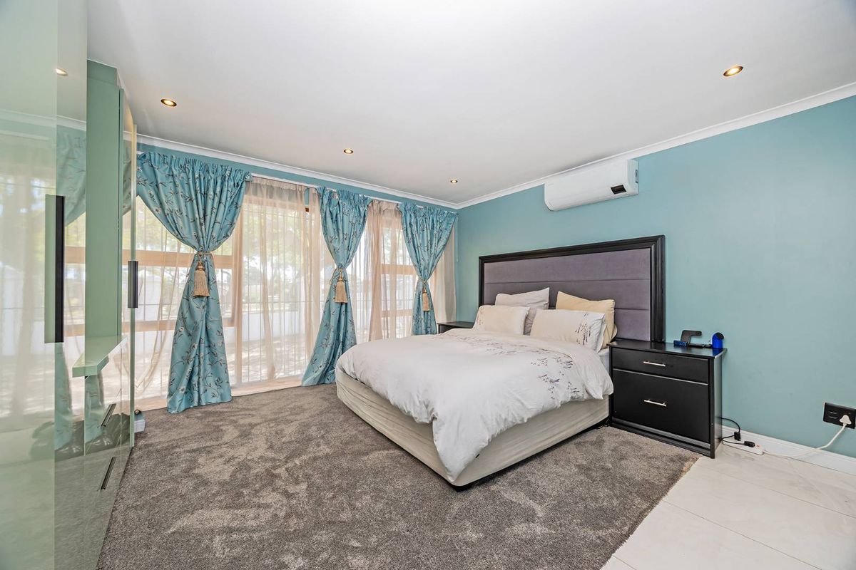 Spacious bedroom featuring a wall-mounted air conditioning unit, large sliding glass doors with curtains, and recessed ceiling lighting.