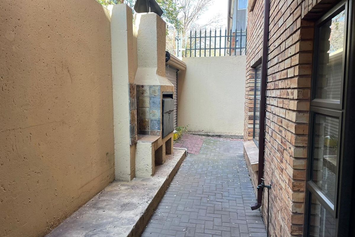 A private outdoor courtyard featuring a built-in brick braai fireplace, paved flooring, and perimeter walling with security spikes.