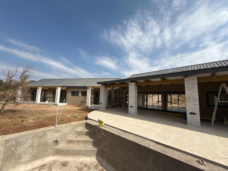 Rear view of a modern house under construction, featuring a large covered patio, stone-clad pillars, and an unfinished swimming pool area.