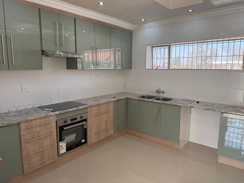 Modern kitchen featuring sage green and wood-grain cabinetry, stone-look laminate countertops, integrated oven and hob, and tiled flooring.