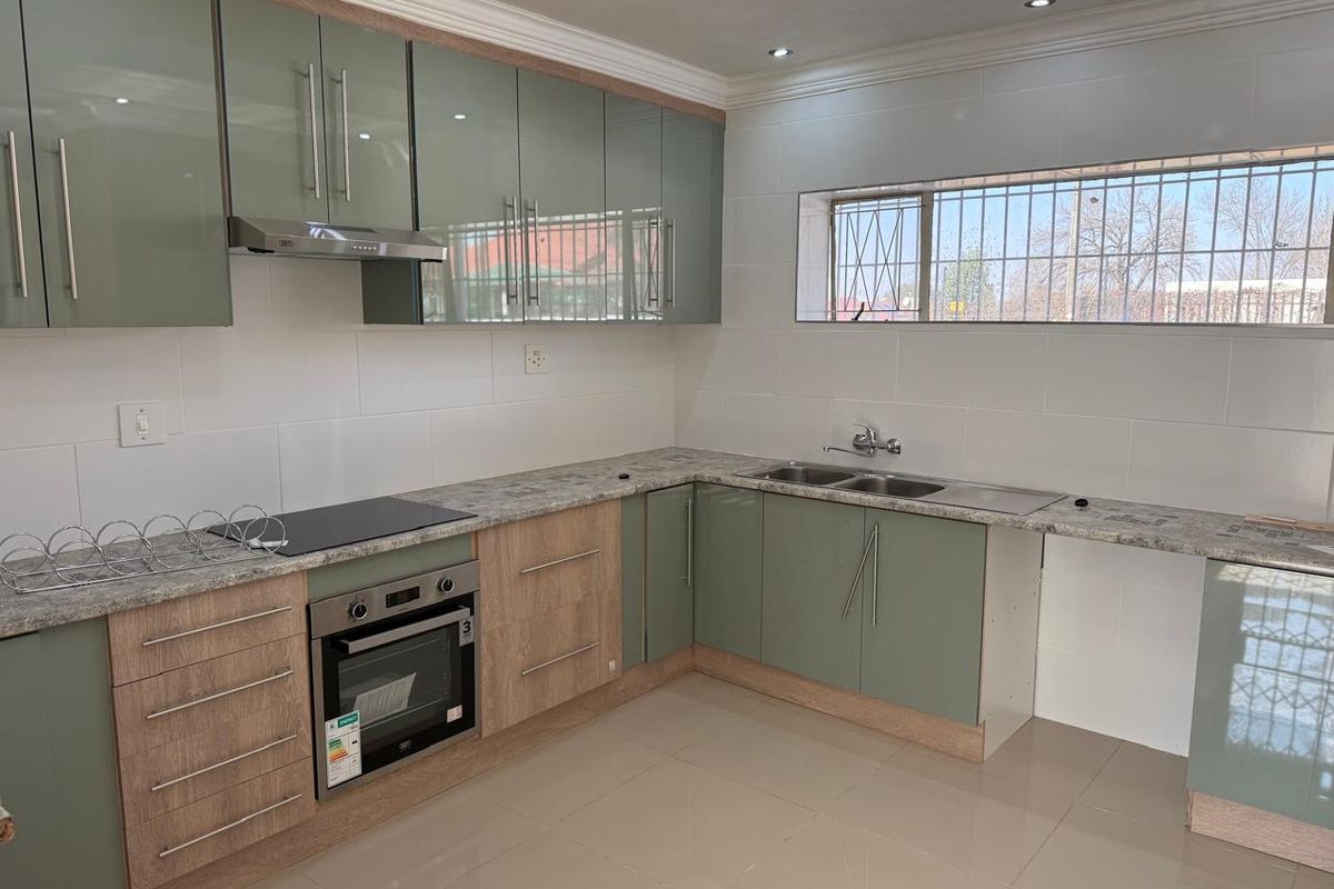Modern kitchen featuring sage green and wood-grain cabinetry, stone-look laminate countertops, integrated oven and hob, and tiled flooring.