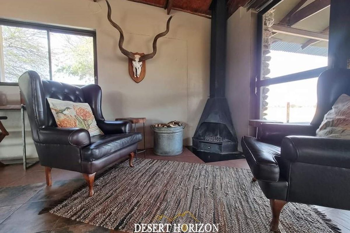 A cozy living area featuring a built-in metal fireplace, exposed timber ceiling beams, and large windows providing natural light and views.