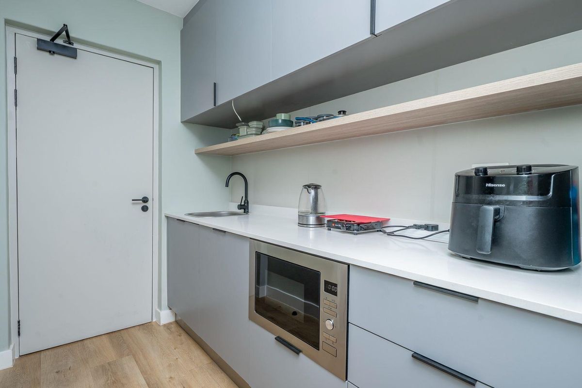 Modern kitchen featuring sleek grey cabinetry, white stone countertops, a built-in microwave, and a minimalist black faucet.
