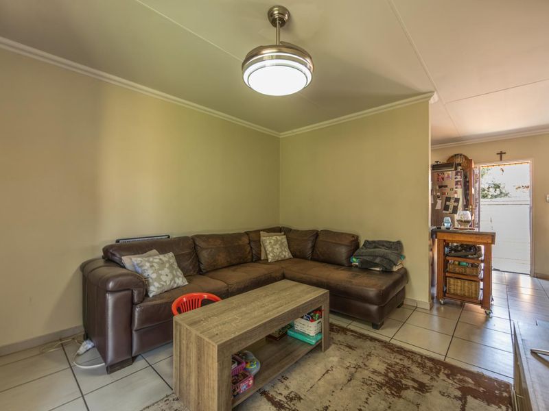 A comfortable living room featuring tiled flooring, coved cornicing, and a central ceiling fan, providing a functional and well-lit space.