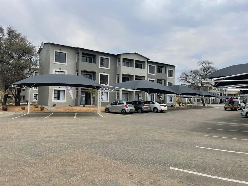 Exterior view of a multi-story apartment complex featuring paved parking bays with shade cloth carports and modern aluminium window frames.