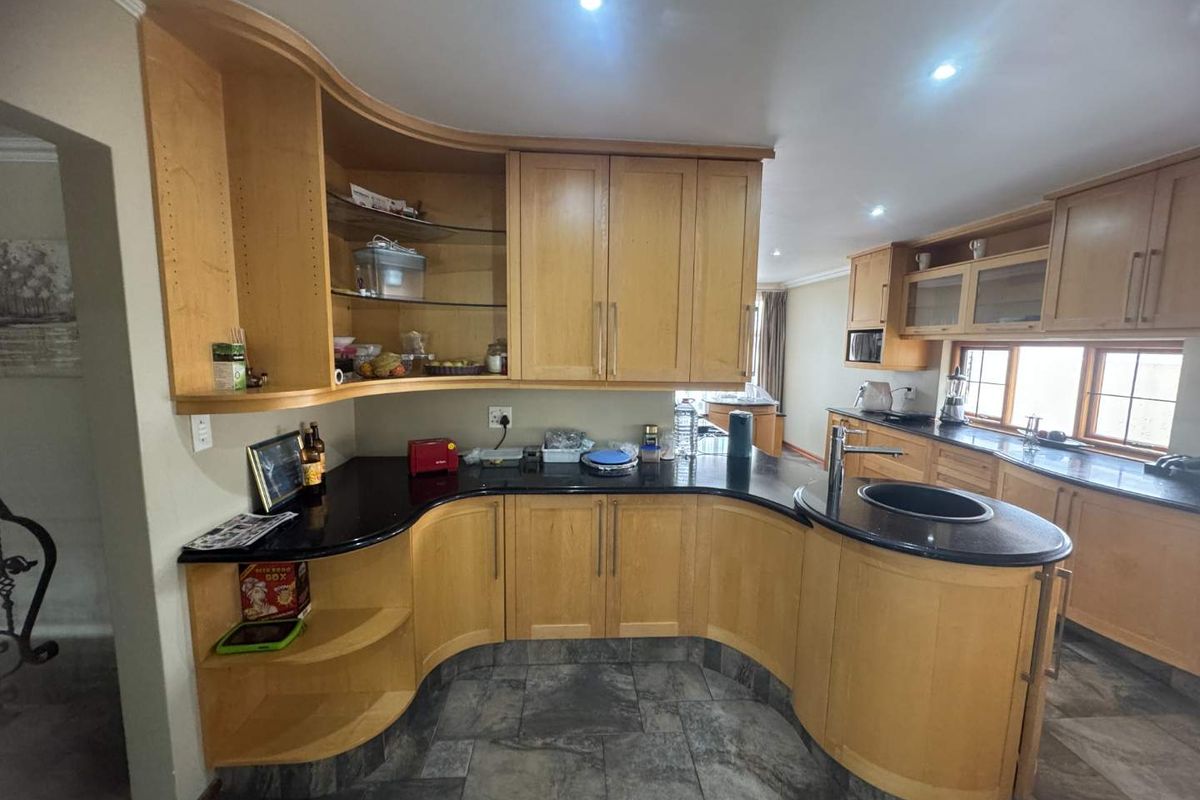 A functional kitchen featuring curved light wood cabinetry, dark granite countertops, integrated sink, and tiled flooring with recessed ceiling lighting.