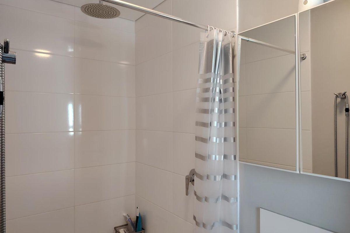 A clean, functional bathroom featuring a modern rain shower head, handheld shower attachment, and a practical wall-mounted mirror cabinet with tiled walls.