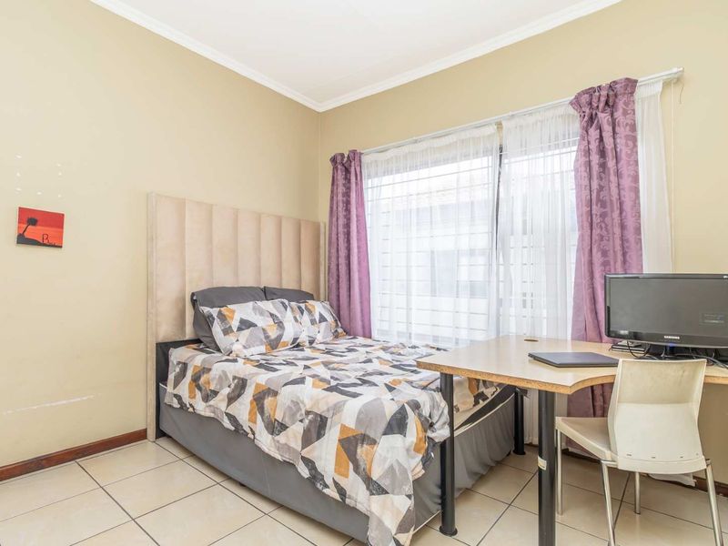 A functional bedroom featuring tiled flooring, a large window with natural light, and neutral wall finishes.