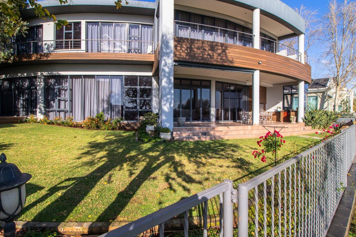 A modern two-story residence featuring a curved architectural design, expansive glass sliding doors, a covered patio, and a well-maintained lawn.