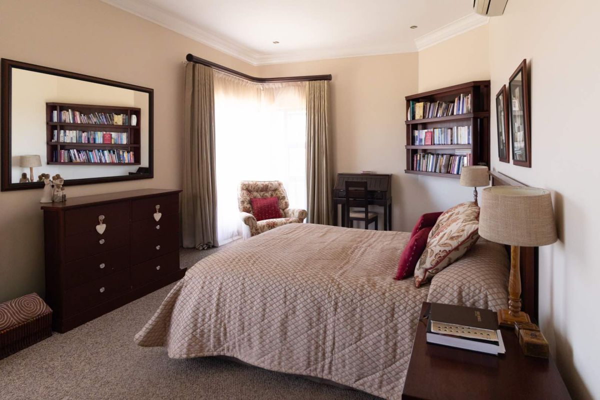 A well-maintained bedroom featuring built-in shelving, a bay window with curtains, and neutral carpeting.
