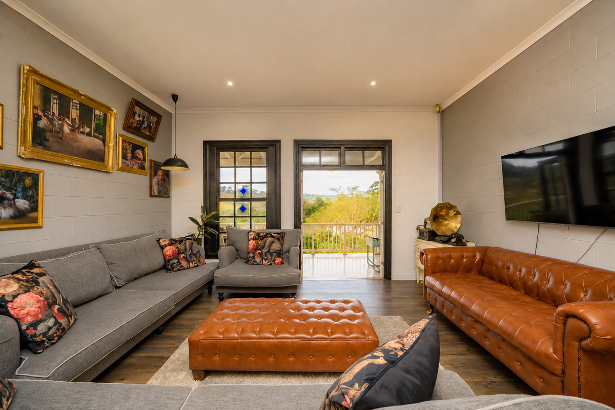 A well-maintained living room featuring painted blockwork walls, recessed lighting, and direct access to an outdoor balcony with scenic views.