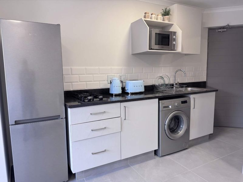 A compact, modern kitchen featuring white cabinetry, granite countertops, subway tile backsplash, and integrated appliances including a gas hob and washing machine.