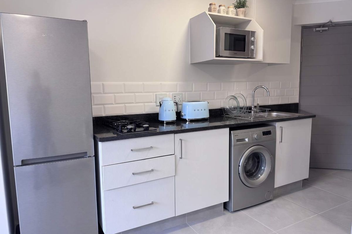 A compact, modern kitchen featuring white cabinetry, granite countertops, subway tile backsplash, and integrated appliances including a gas hob and washing machine.