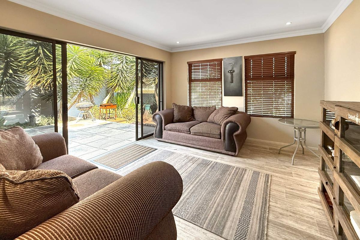 A bright living room featuring large sliding glass doors that open onto a paved patio area, with tiled flooring and wooden blinds.
