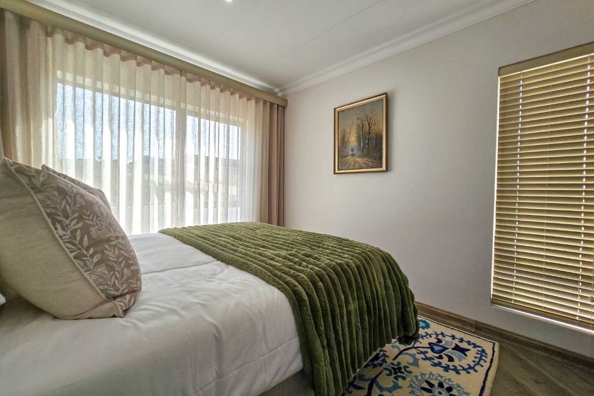 A well-maintained bedroom featuring neutral walls, recessed ceiling lighting, large windows with sheer curtains, and fitted wooden blinds.