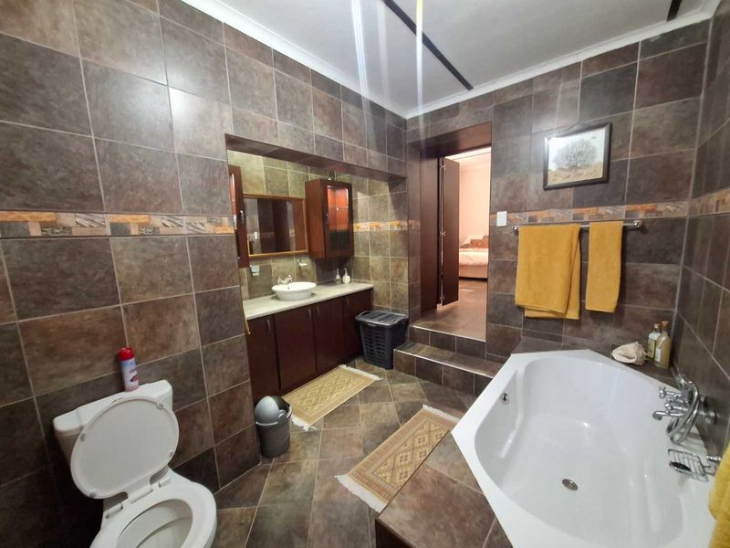 A spacious bathroom featuring dark tiled walls and flooring, a built-in vanity with a vessel sink, and a corner bathtub.