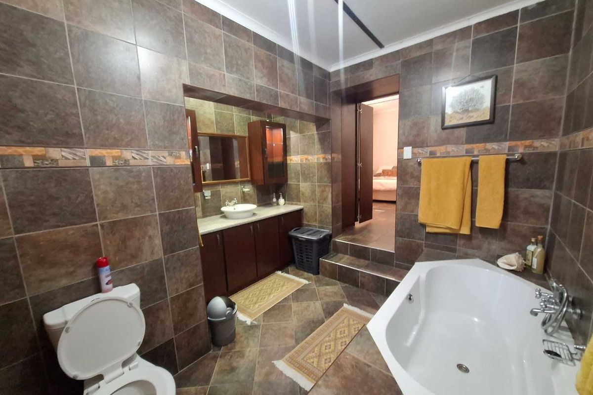 A spacious bathroom featuring dark tiled walls and flooring, a built-in vanity with a vessel sink, and a corner bathtub.
