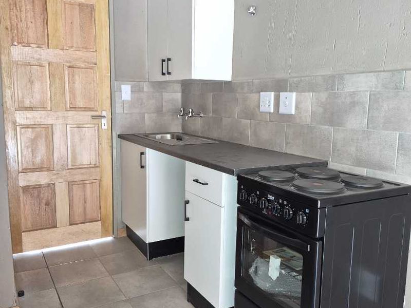 A compact kitchen featuring white cabinetry, a stainless steel sink, tiled backsplash, and a freestanding electric stove with tiled flooring.