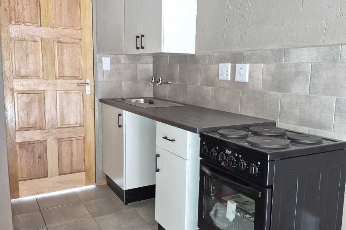 A compact kitchen featuring white cabinetry, a stainless steel sink, tiled backsplash, and a freestanding electric stove with tiled flooring.