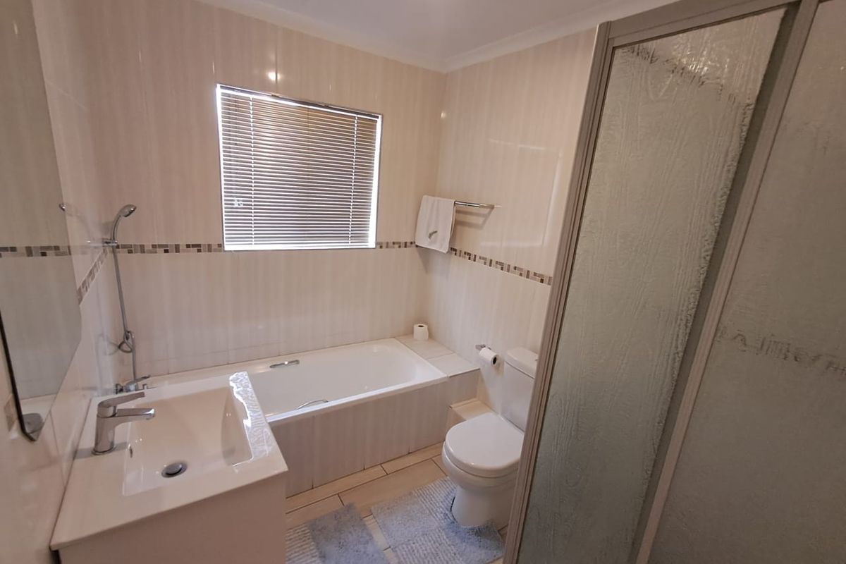 A functional bathroom featuring a built-in bathtub, a separate shower enclosure, a vanity basin, and a toilet with neutral wall tiling.