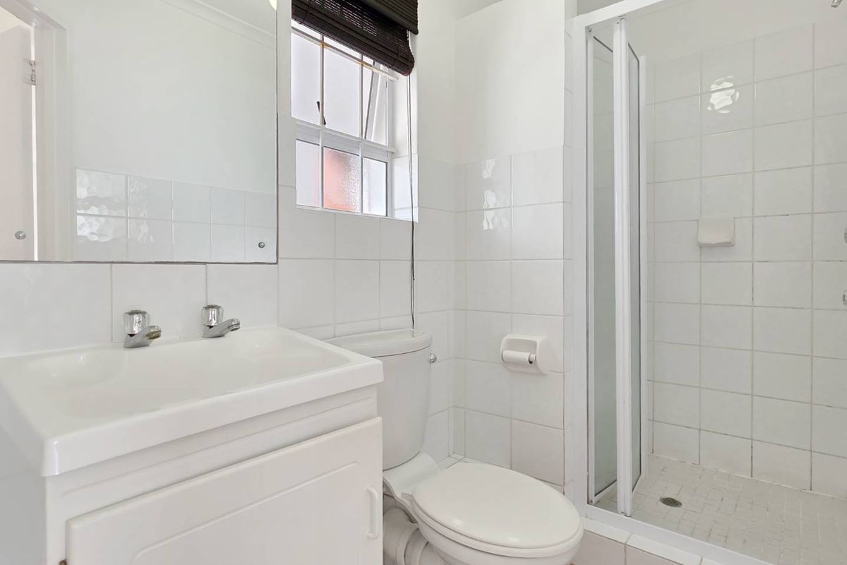 A functional bathroom featuring a white vanity, toilet, and a glass-enclosed shower with white wall tiling.