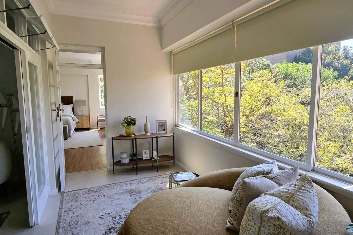 A bright sunroom or living area featuring large picture windows with garden views, crown molding, and double glass doors leading to the bedroom.