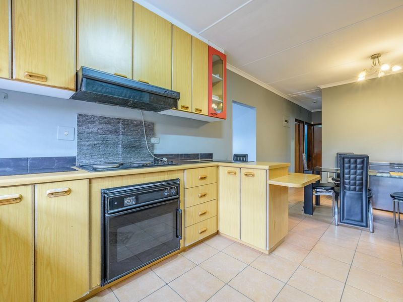 A functional kitchen featuring light wood cabinetry, built-in oven and hob, extractor fan, and tiled flooring, with an open-plan layout leading to the dining area.